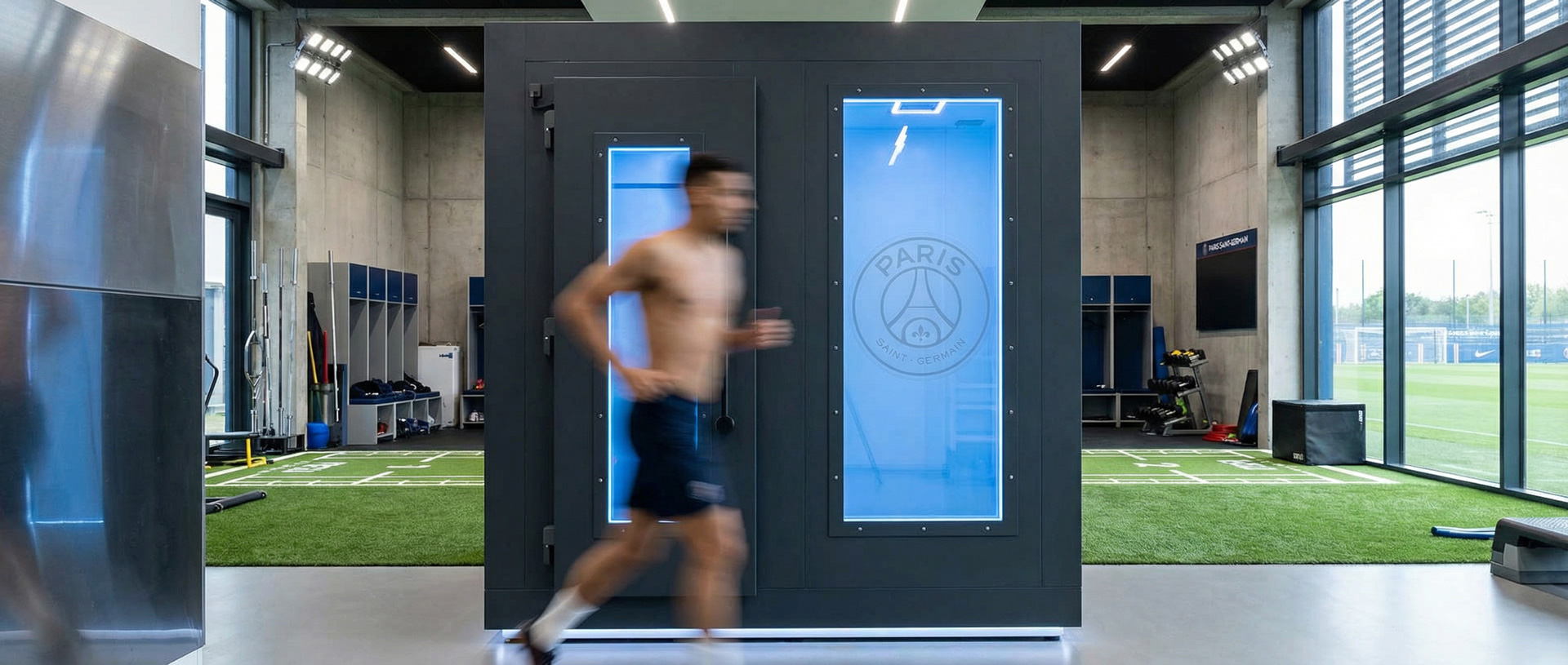Ein Sportler läuft an einer schwarzen LifeCube Kältekammer mit beleuchtetem PSG-Logo in einem modernen Fitnessraum vorbei.